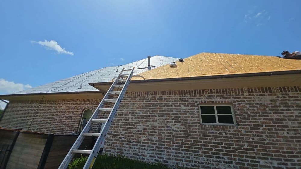 Roofing project with a ladder, newly installed shingles, and clear blue sky.