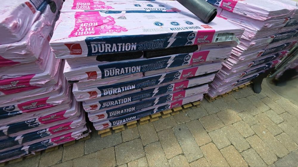 Colorful Duration Storm roofing shingles stacked on wooden pallets outdoors. Ideal for home renovations.