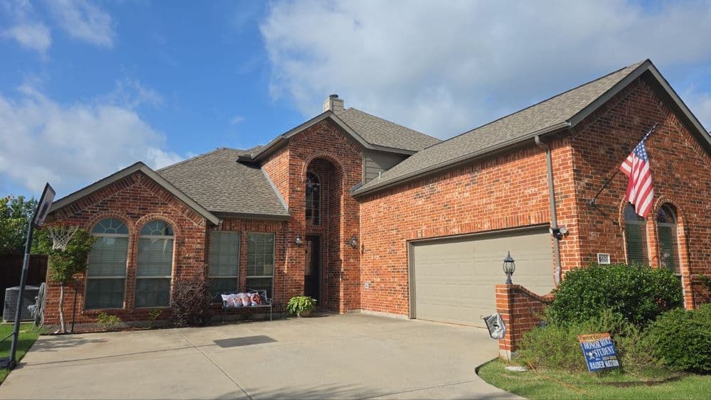 Brick home with landscaped front yard, American flag, and basketball hoop in a sunny neighborhood.