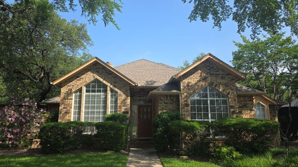 Brick home with large windows, manicured shrubs, and blooming flowers under a blue sky.